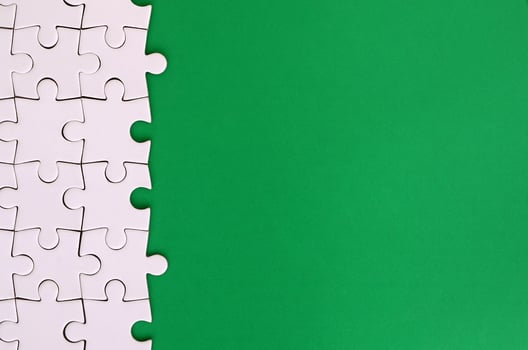Fragment of a folded white jigsaw puzzle on the background of a green plastic surface. Texture photo with copy space for text