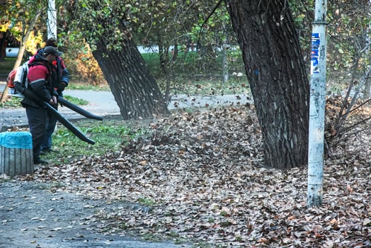 Dnipro, Ukraine - 10.30.2021 Workers on the street in autumn collects leaves with a blower photo
