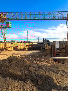 gantry crane to create a metro in the city center. the crane works in the ground, digs long paths. people build a road and rails for high-speed trains. against the blue blue sky photo