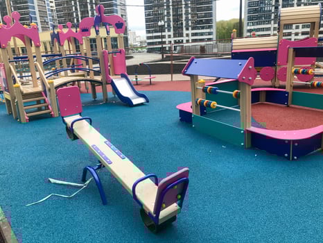 children's pink playground in the center of the residential complex. there are swings, slides and climbing frames for kids. double swing for children to ride. playground next to tall glass blue houses photo