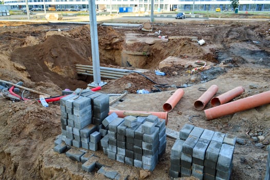 asphalt bricks lie at a construction site. small gray bricks are stacked flat on a construction site in the city center. nearby are metal pipes and a sand ditch. large construction site photo