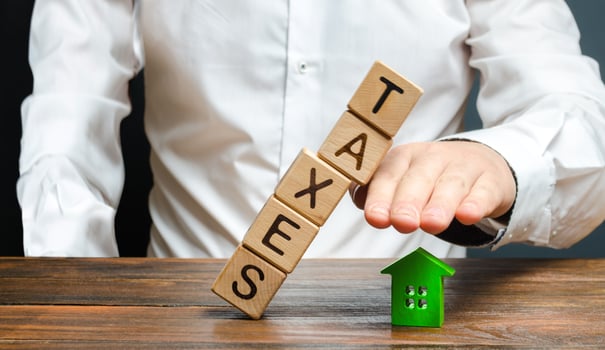 A man protects his hand with a figurine of a house from a falling tower of cubes with the word taxes. Heavy tax burden, protecting the interests of small and medium-sized businesses, competitiveness. photo