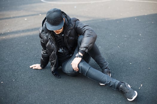 Young stylish guy in black fashionable clothes sitting on the pavement photo