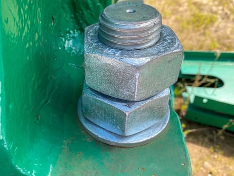 Two nuts are screwed onto a large iron metal stainless mounted threaded bolt. Close view photo