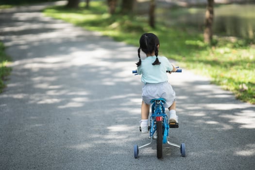 back side view of asian baby girl child learning to ride bicycle in the park garden. Education concept for kid practiice cycling at park, baby sport concept. photo