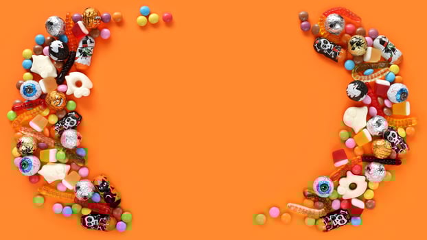 Halloween orange banner, copy space in middle. Assorted candies half rounds on both sides - traditional eyeballs chocolates, jelly worms, gummy ghosts. Happy Halloween holiday trick-or-treat concept. photo