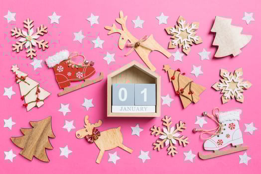 Top view of calendar, pink background decorated with festive toys and Christmas symbols reindeers and New Year trees. The first of January. Holiday concept photo