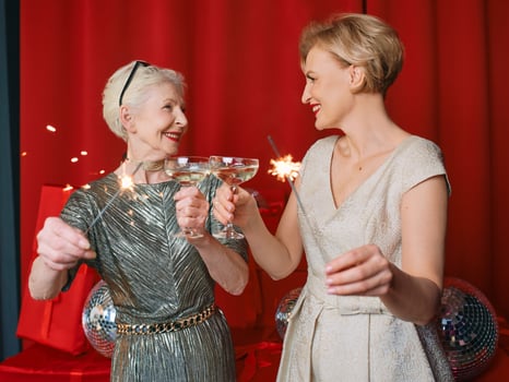 Two beautiful stylish mature senior women in dresses with sparklers and glasses celebrating new year. Christmas, family, friends, new year, Fun, party, style, celebration concept photo