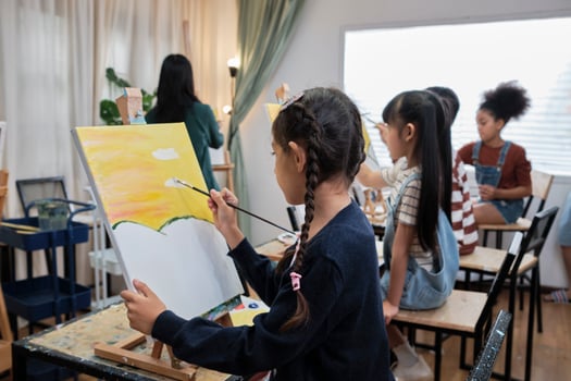 A group of multiracial kids learning with a female Asian teaches acrylic color picture painting on canvas in art classroom, creatively learning with skill at the elementary school studio education. photo