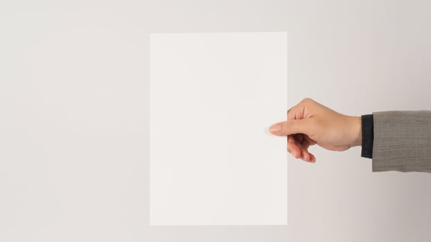 Space for text. The hand is wearing a gray suit and holding blank board A4 paper on white background. photo