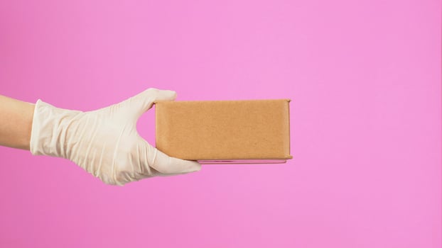 The hand is holding a brown box isolated on pink background.side view photo