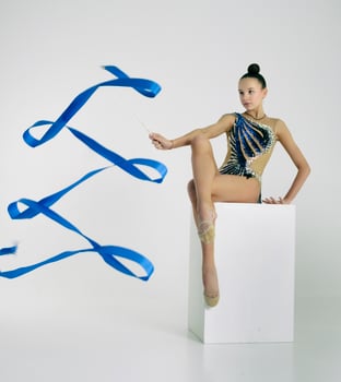 a girl from rhythmic gymnastics in a bodysuit rotates a ribbon while sitting on a cube photo