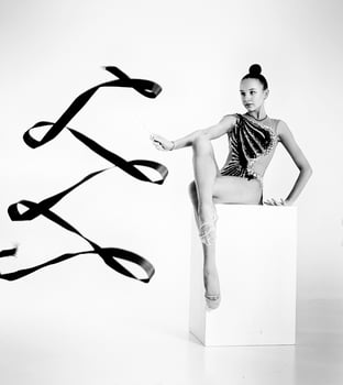girl from rhythmic gymnastics, in a bodysuit rotates a ribbon while sitting on a cube photo