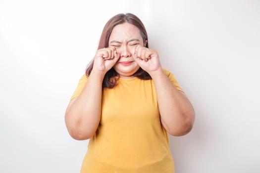 A portrait of an Asian big sized woman wearing a yellow t-shirt isolated by white background looks depressed photo