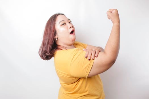 Excited Asian big sized woman wearing a yellow t-shirt showing strong gesture by lifting her arms and muscles smiling proudly photo