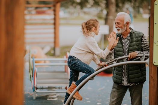 Grandfather spending time with his granddaughter in park playground on autumn day photo