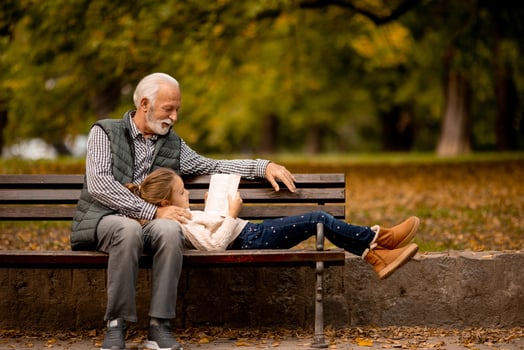 Grandfather spending time with his granddaughter on bench in park on autumn day photo