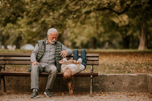 Grandfather spending time with his granddaughter on bench in park on autumn day photo