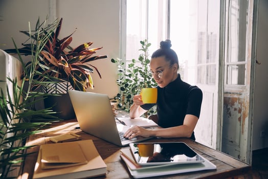 Confident woman using laptop and enjoying hot drink while sitting at her working place in office photo