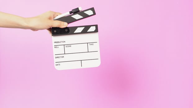 Hand is holding clapper board and marker pen on pink background. photo