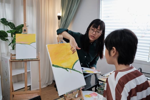 Female Asian teacher teaches and demonstrates to the student boy on acrylic color picture painting on canvas in art classroom, creatively learning with skill at the elementary school studio education. photo