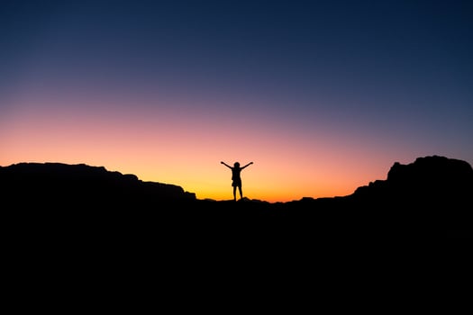 Happy celebrating winning success woman at sunset or sunrise standing elated with arms raised up in celebration of having reached mountain top summit goal during hiking travel trek photo
