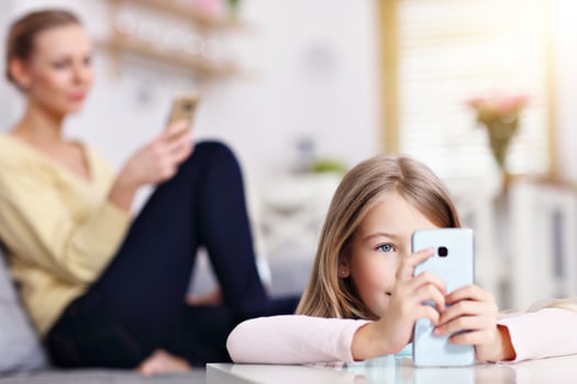 Young mom and her little daughter using smartphone and sitting on sofa at home photo
