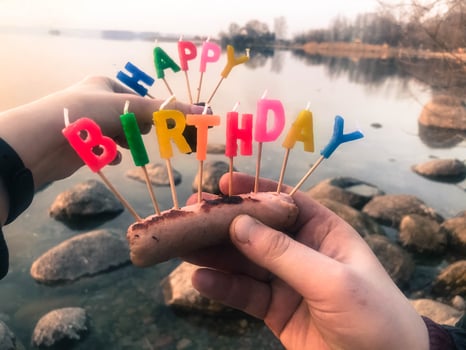 Happy birthday inscription made of holiday candles in the hands of a man and a woman opposite the water of the ocean lake river photo
