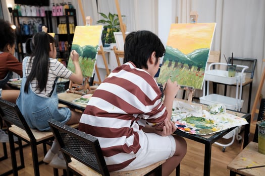 A group of student kids concentrates on acrylic color picture painting with a paintbrush on canvas in art classroom, creatively learning with talents and skills at elementary school studio education. photo