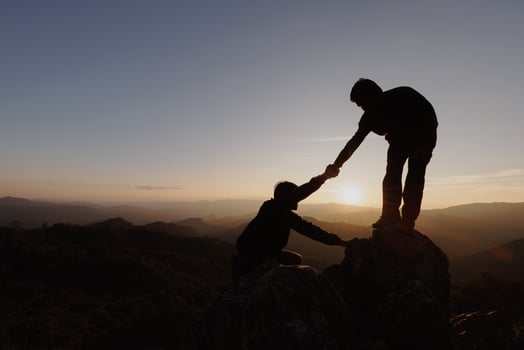 Silhouettes of two people climbing on mountain and helping. Help and assistance concept. photo