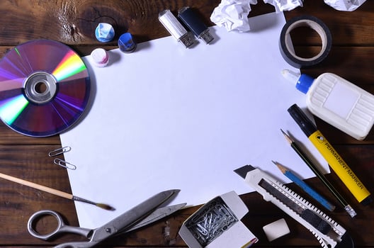 A school or office still life with a white blank sheet of paper and many office supplies. The school supplies lie on a brown wooden background. Place for text photo