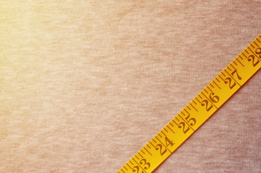 Yellow measuring tape lies on a gray knitted fabric photo