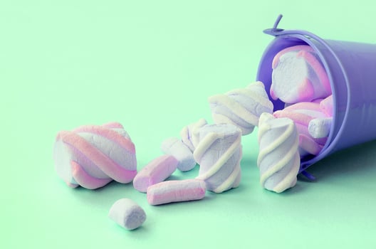Overturned miniature lilac bucket filled with marshmallow lies on a turquoise pastel background photo
