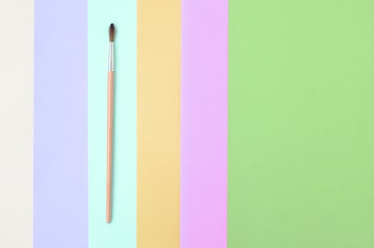 A new paint brush lie on texture background of fashion pastel pink, blue, green, yellow, violet and beige colors paper photo