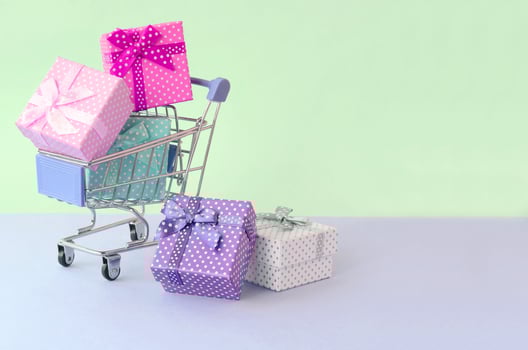 Small gift boxes of different colors with ribbons in shopping cart on a violet and blue pastel background photo