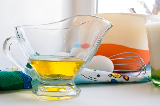 sunflower oil in a glass transparent oiler on a white windowsill next to the ingredients for pancakes, close up photo