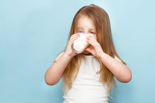 little beautiful girl drinking milk in glass on a blue background photo