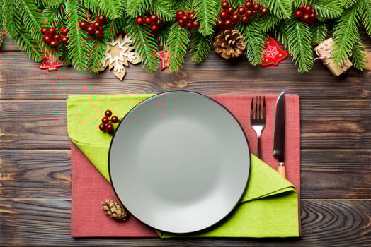 Top view of cutlery and plate on festive wooden background. New Year family dinner concept. Fir tree and Christmas decorations photo