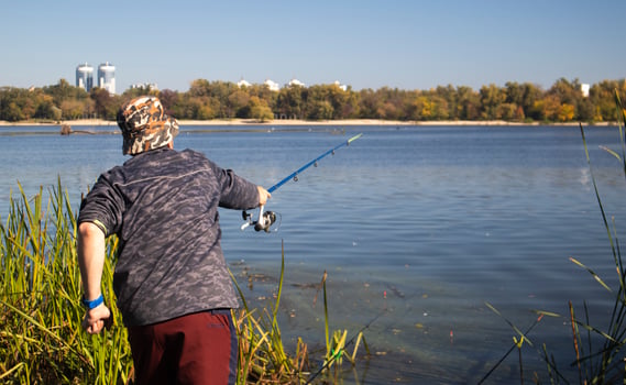 A male fisherman threw a spinning rod into a lake or river on a sunny day. Shore fishing. A fisherman on the river bank holds a spinning rod in his hand. The concept of country rest. Fishing article. photo