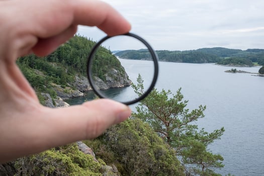 Photographer hand puts a polarization filter on the camera, against the backdrop of a beautiful landscape of the sea and rocks. photo