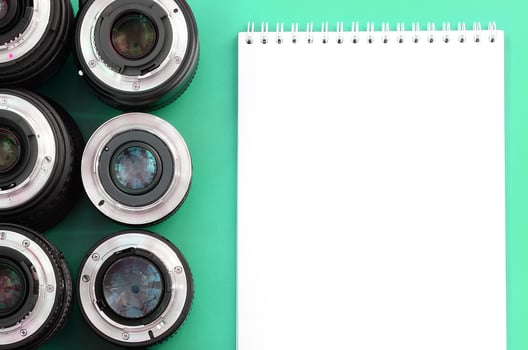 Several photographic lenses and white notebook lie on a bright turquoise background. Copy space photo