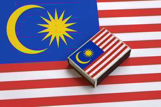 Malaysia flag is pictured on a matchbox that lies on a large flag photo