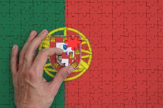Portugal flag is depicted on a puzzle, which the man's hand completes to fold photo