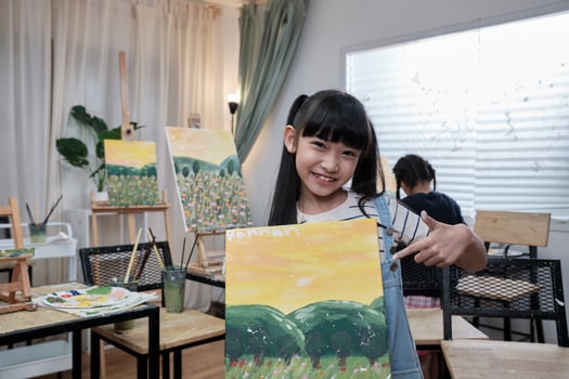 One Asian student girl shows her painting work, proud with portfolio, acrylic color picture on canvas in art classroom and creative learning with talents skill at elementary school studio education. photo