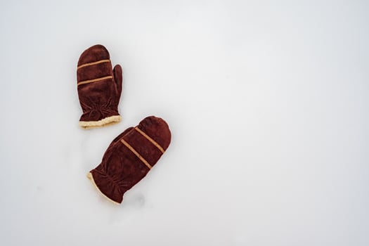 Warm suede brown mittens lie on the pure white snow on a cloudy winter day. Copy space. Top view. photo