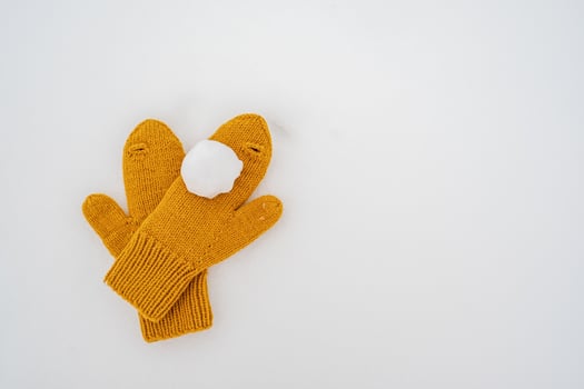 Snowball on yellow knitted mittens, in the snow. Winter active games and entertainment. Copy space. photo