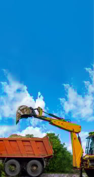 Orange excavator unloads sand from a dump truck. Dig in the agricultural area. photo