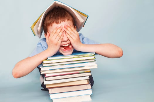 schoolboy sitting with pile of school books and covers his face with hands isolated on a blue background photo