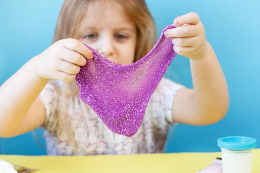 Blonde girl stretching purple slime isolated on blue background. child playing with slime toy. Making slime. Copy space. photo