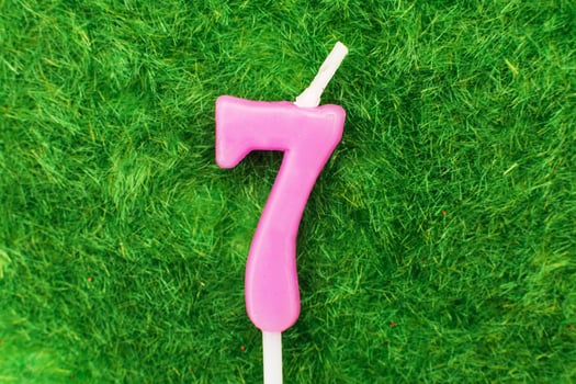 candle in the form of number 7 on the green grass background, a place for a greeting text photo